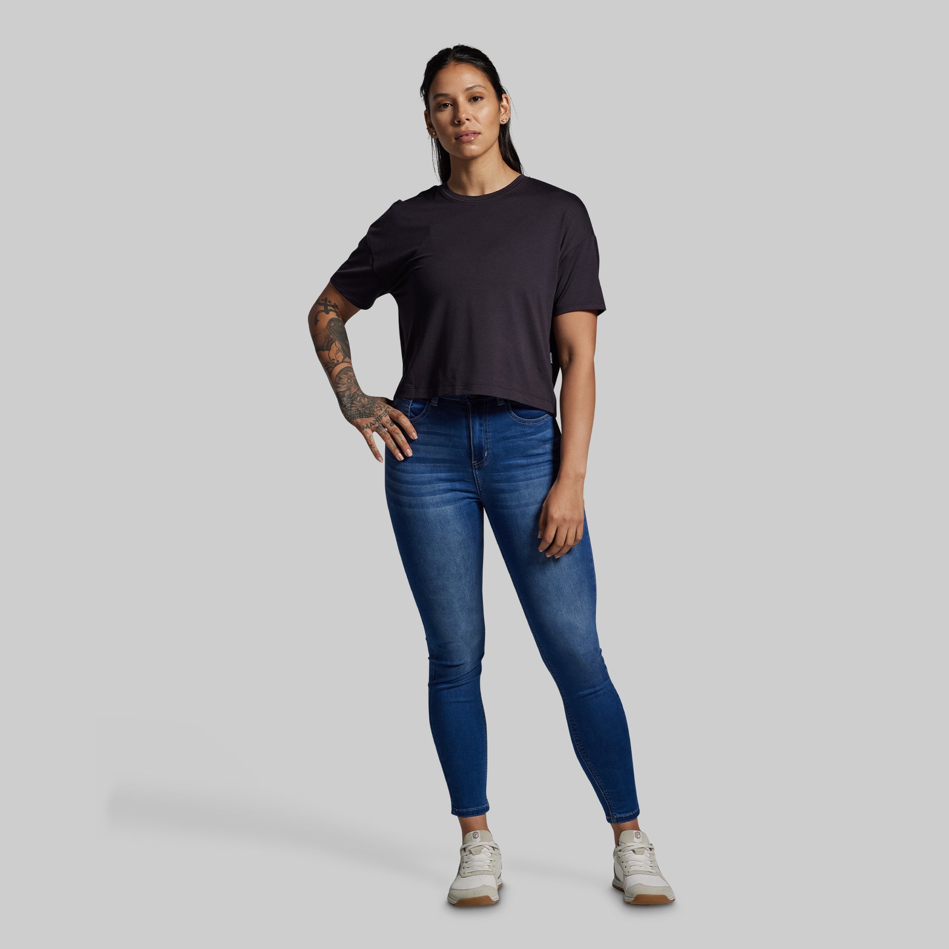 Woman wearing a black t-shirt and blue jeans on a gray background