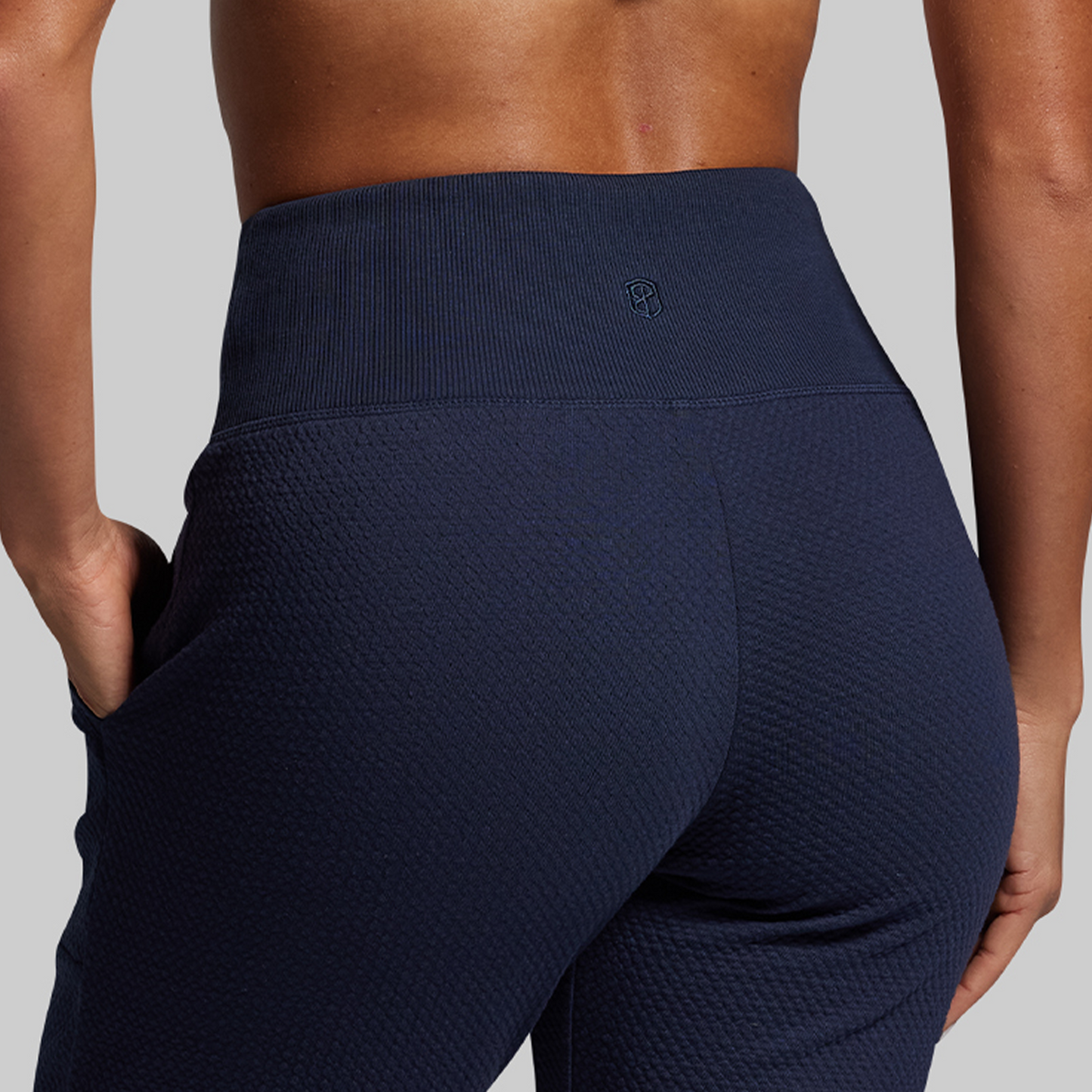 Navy blue textured joggers worn by a person on a gray background
