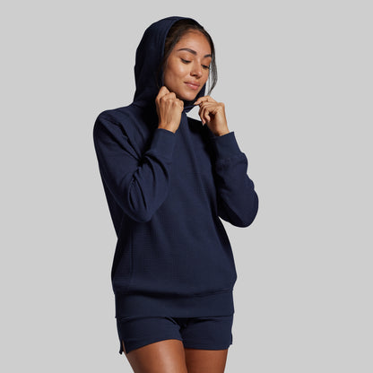 Person wearing a navy blue hoodie and shorts on a gray background
