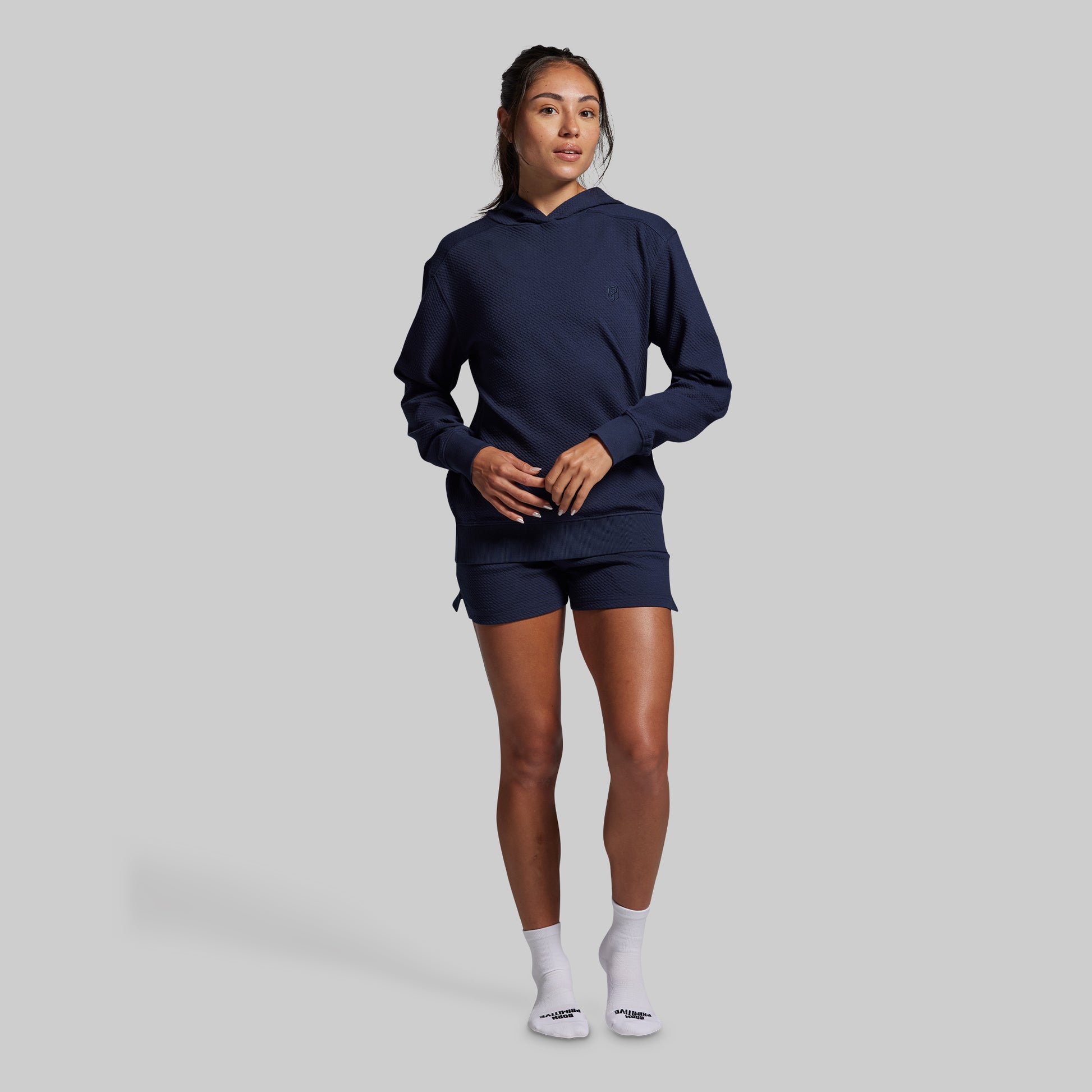 Person wearing a navy blue hoodie and shorts set on a gray background