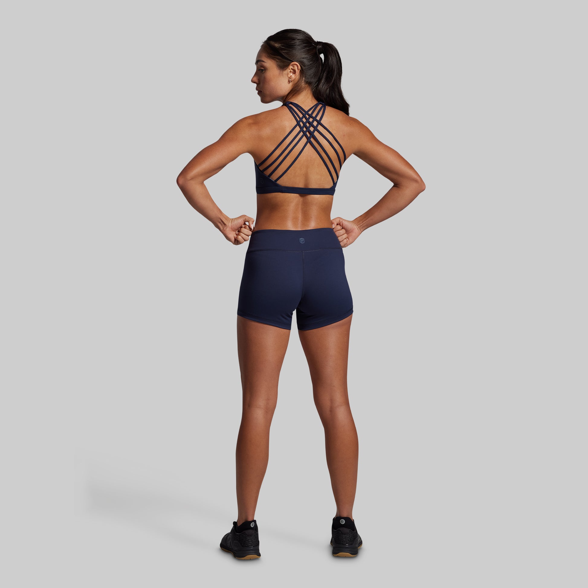 Woman wearing a navy sports bra and shorts on a gray background