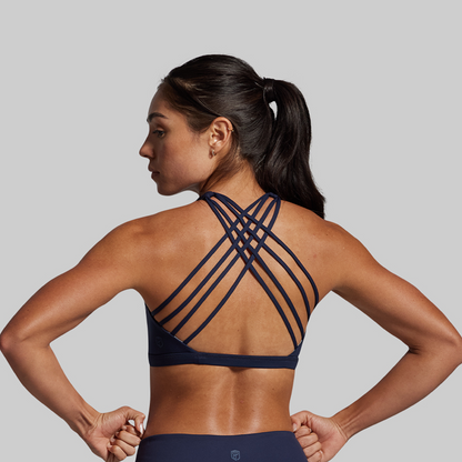 Woman wearing a navy blue sports bra with criss-cross straps on a gray background