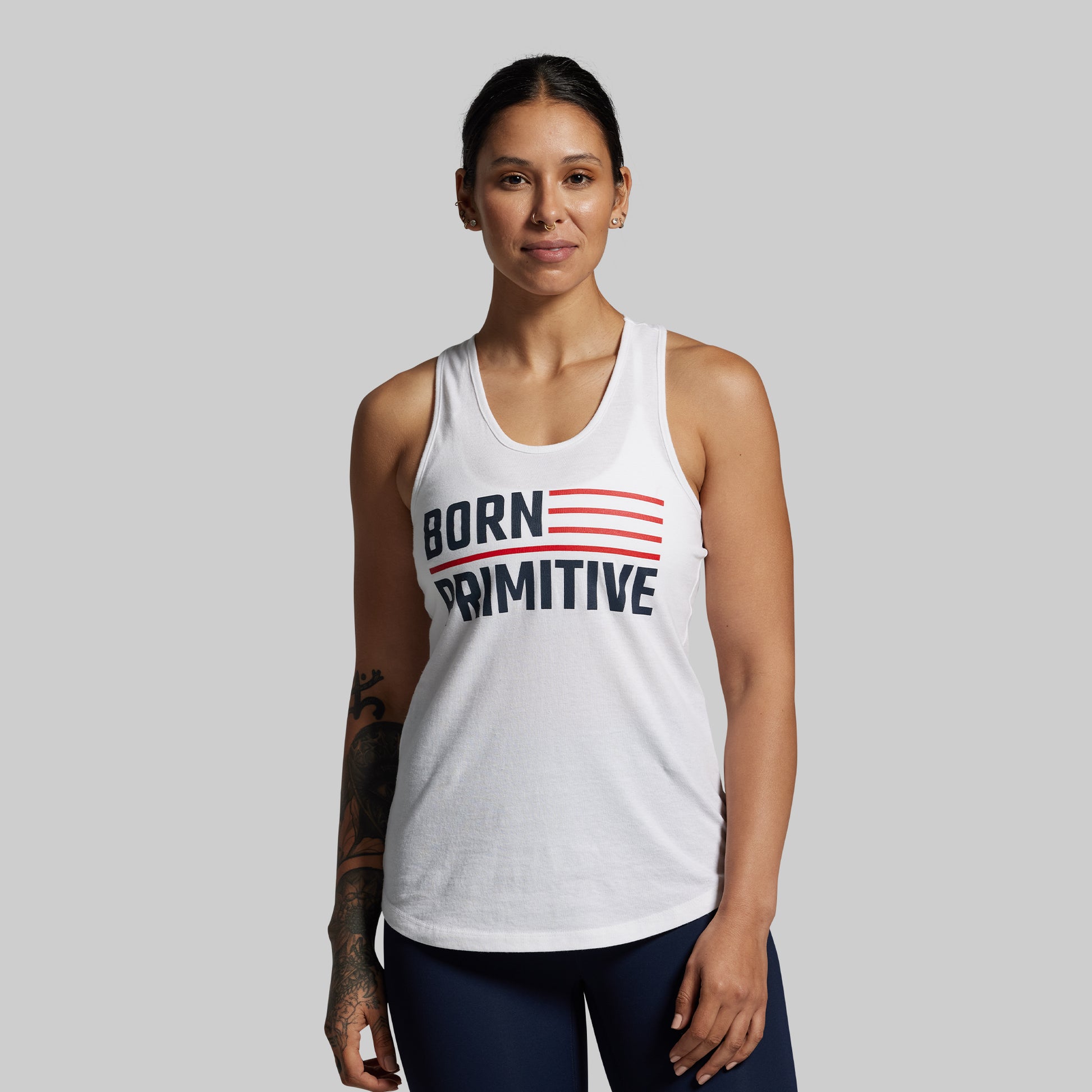 Woman wearing a white tank top with 'Born Primitive' text on a gray background