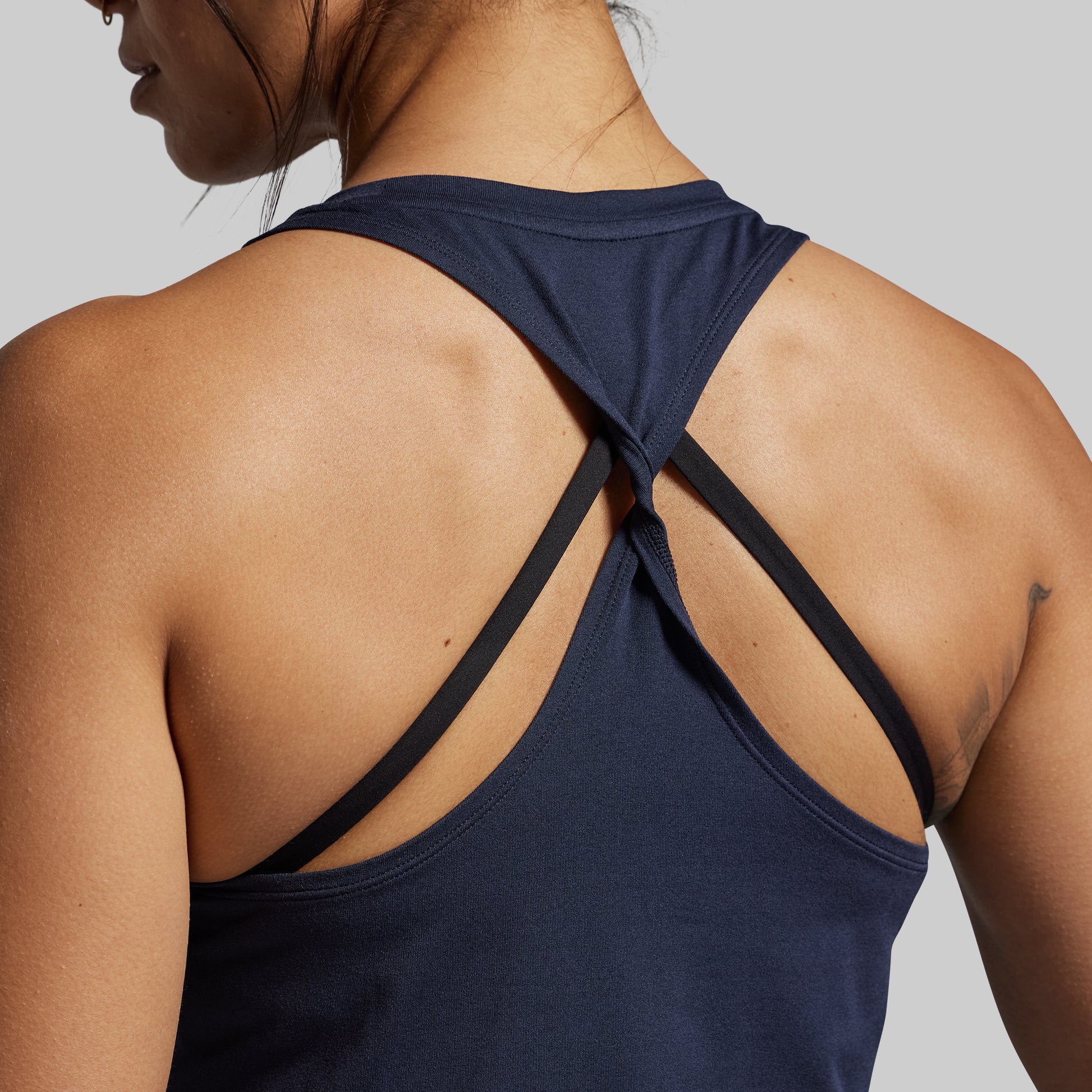 Navy blue tank top with twisted straps worn by a person on a gray background