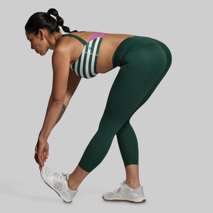 Woman in green athletic leggings and sports bra on a gray background