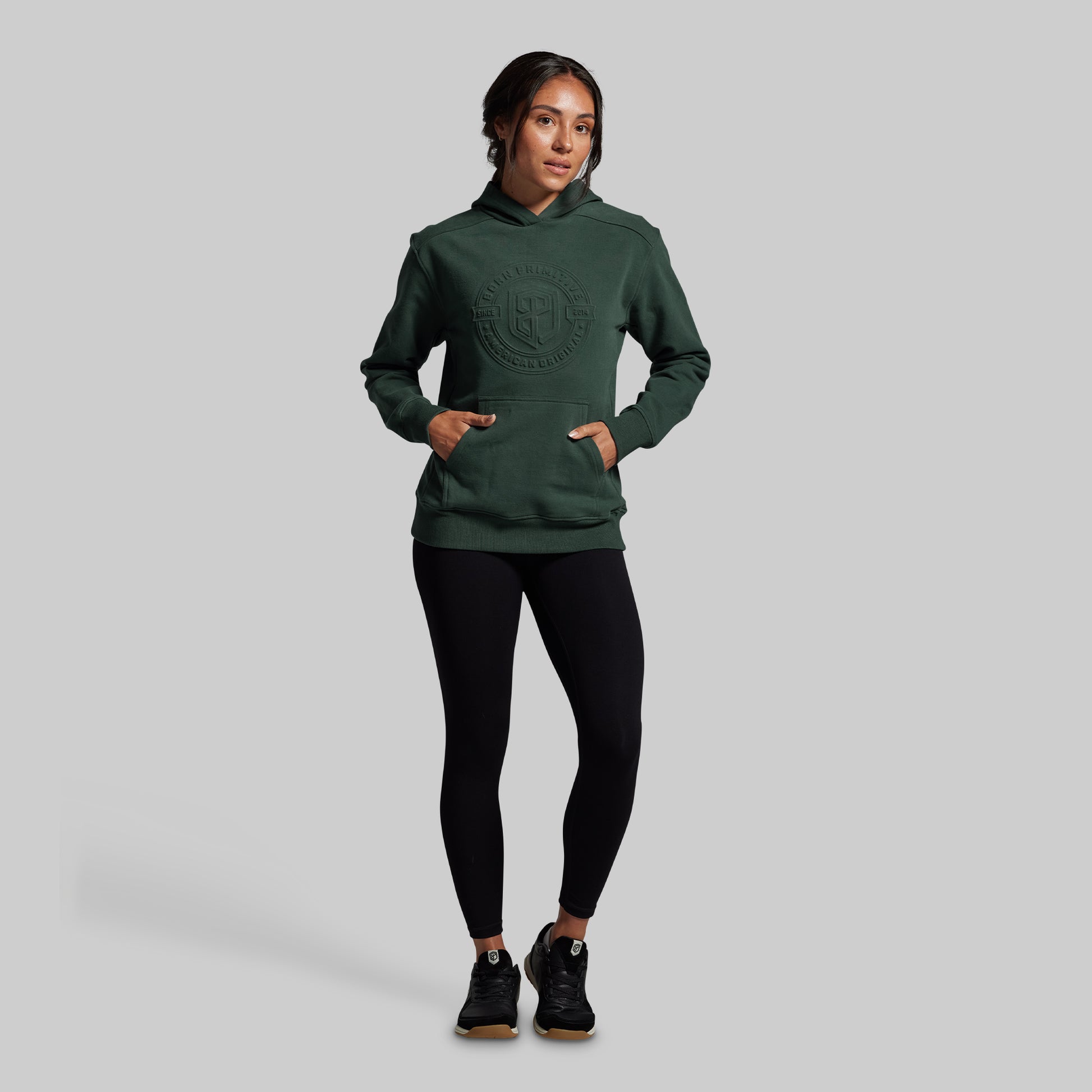 Person wearing a green hoodie and black leggings on a gray background