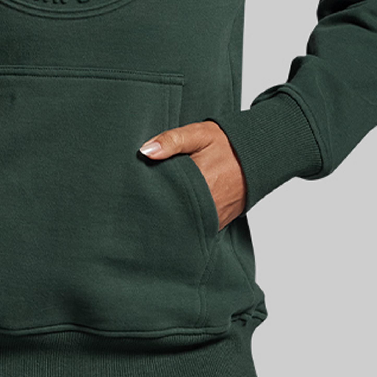 Person wearing a green hoodie with a hand in the pocket against a gray background