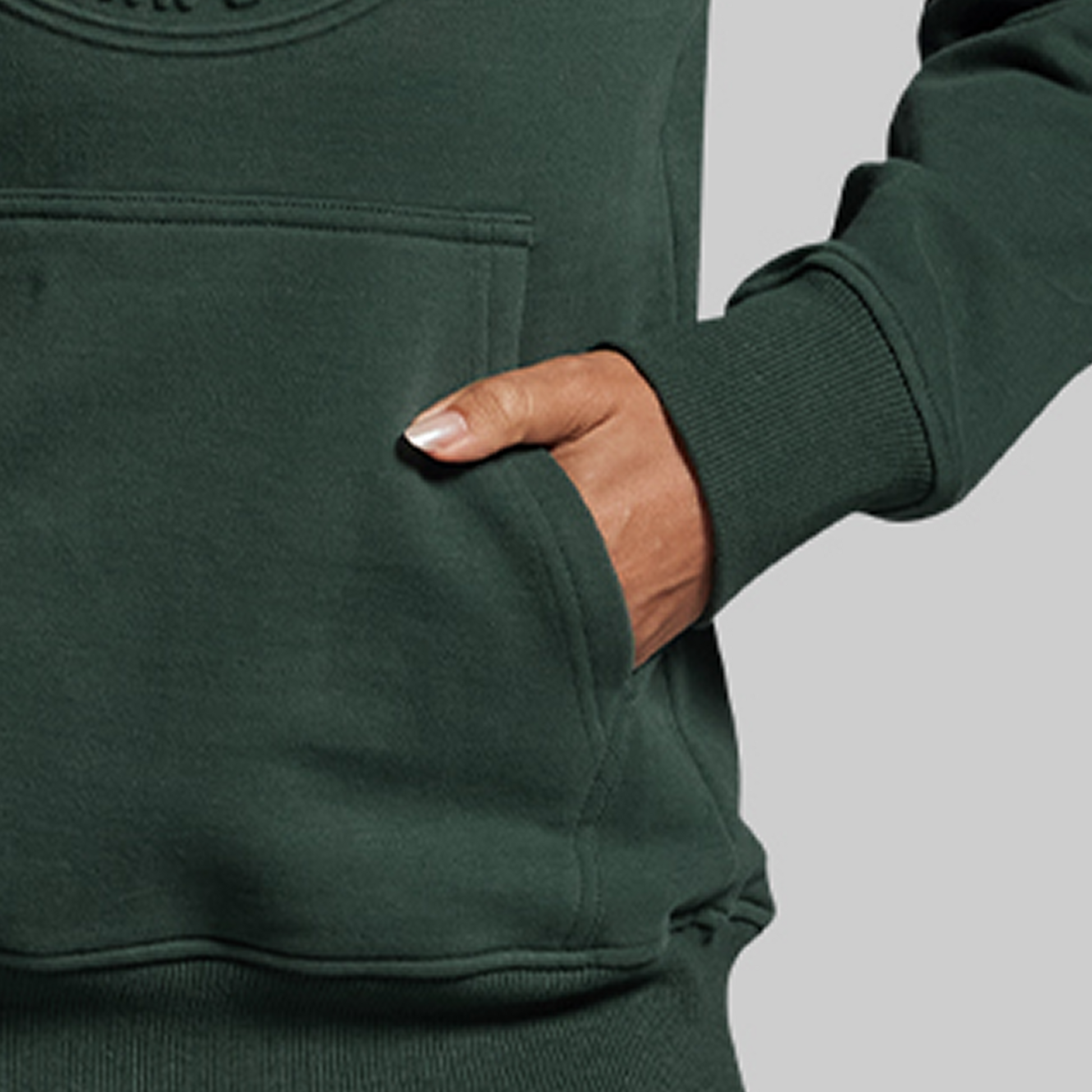 Person wearing a green hoodie with a hand in the pocket against a gray background
