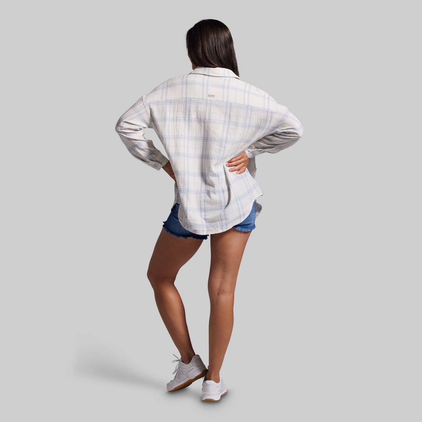 Person wearing a white plaid shirt and denim shorts on a gray background