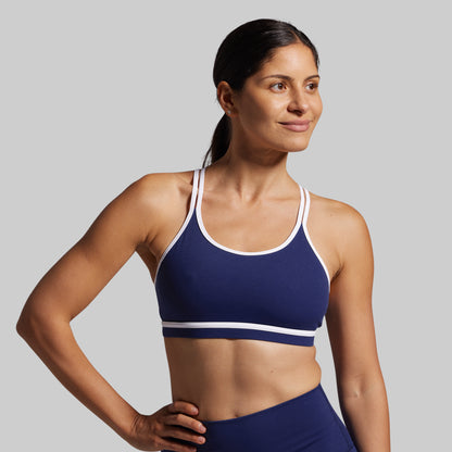 Woman wearing a blue sports bra with white straps on a gray background