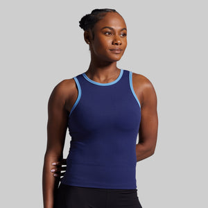 Woman wearing a blue tank top with black pants on a gray background
