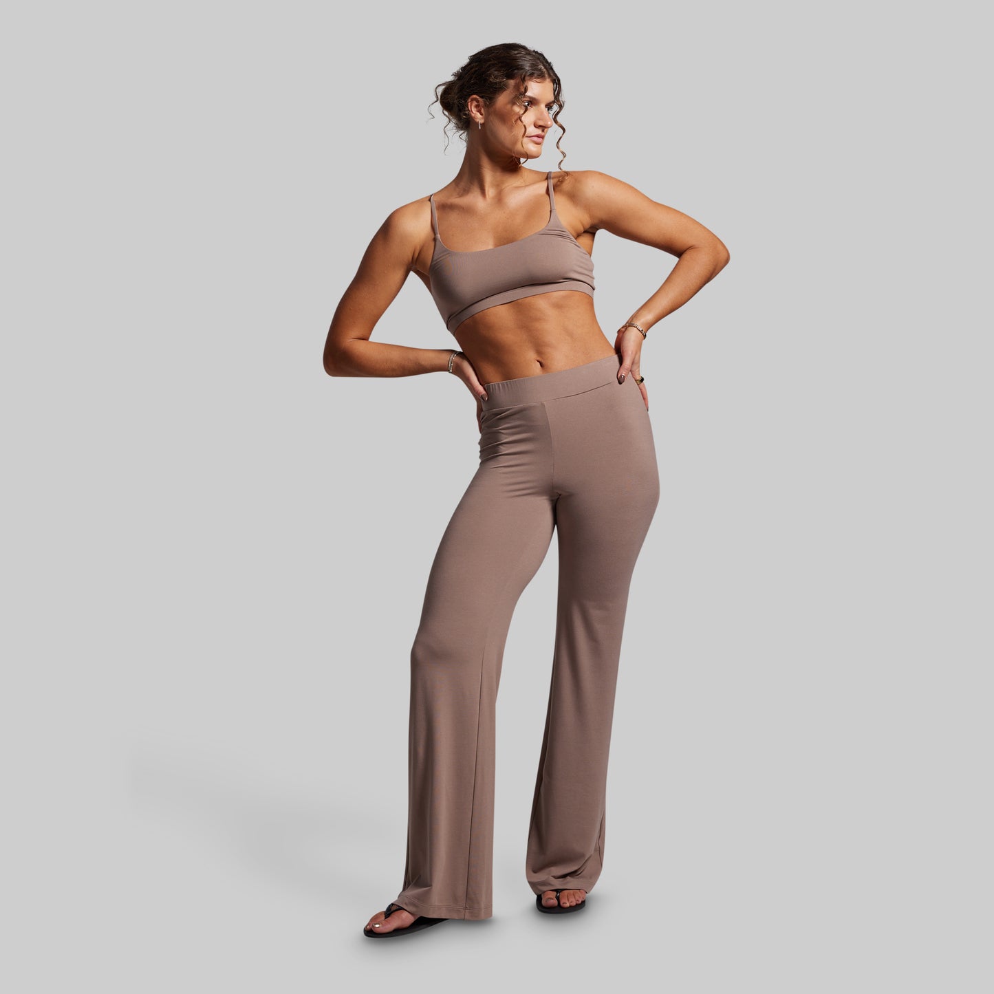 Woman wearing a brown sports bra and pants on a gray background