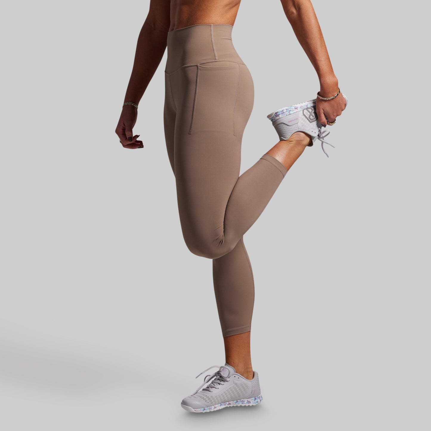 Person wearing beige leggings and gray sneakers on a light gray background