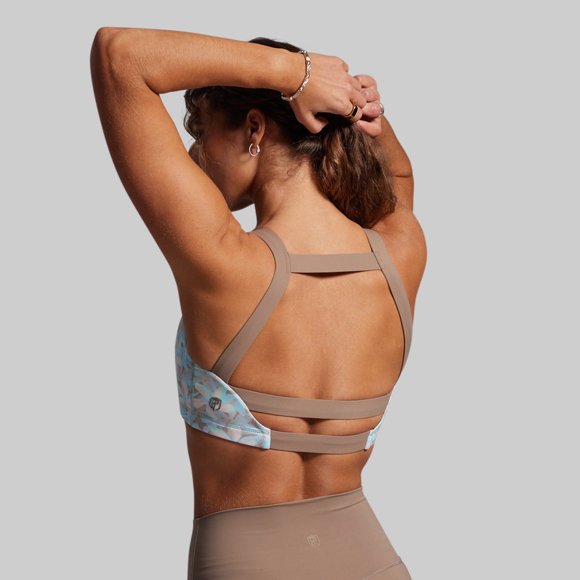 Woman wearing a light blue sports bra with floral pattern and brown straps on a gray background