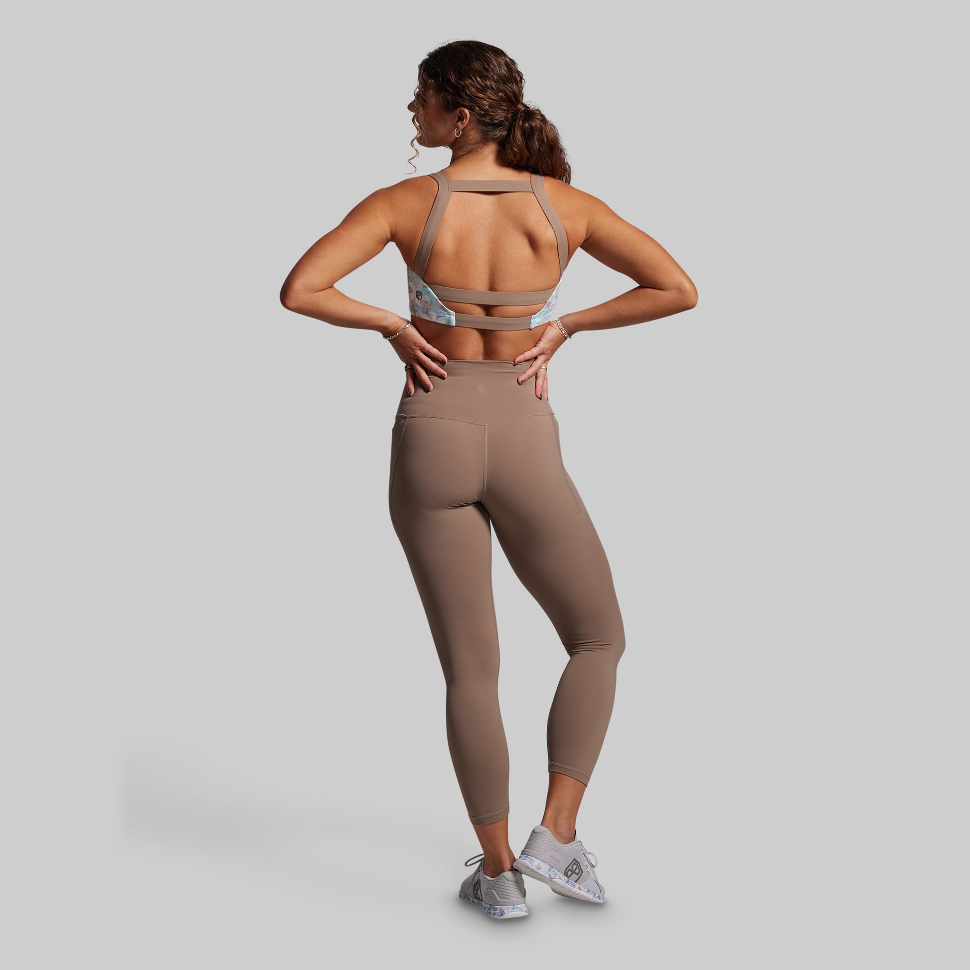 Person wearing a beige sports bra and leggings set on a gray background