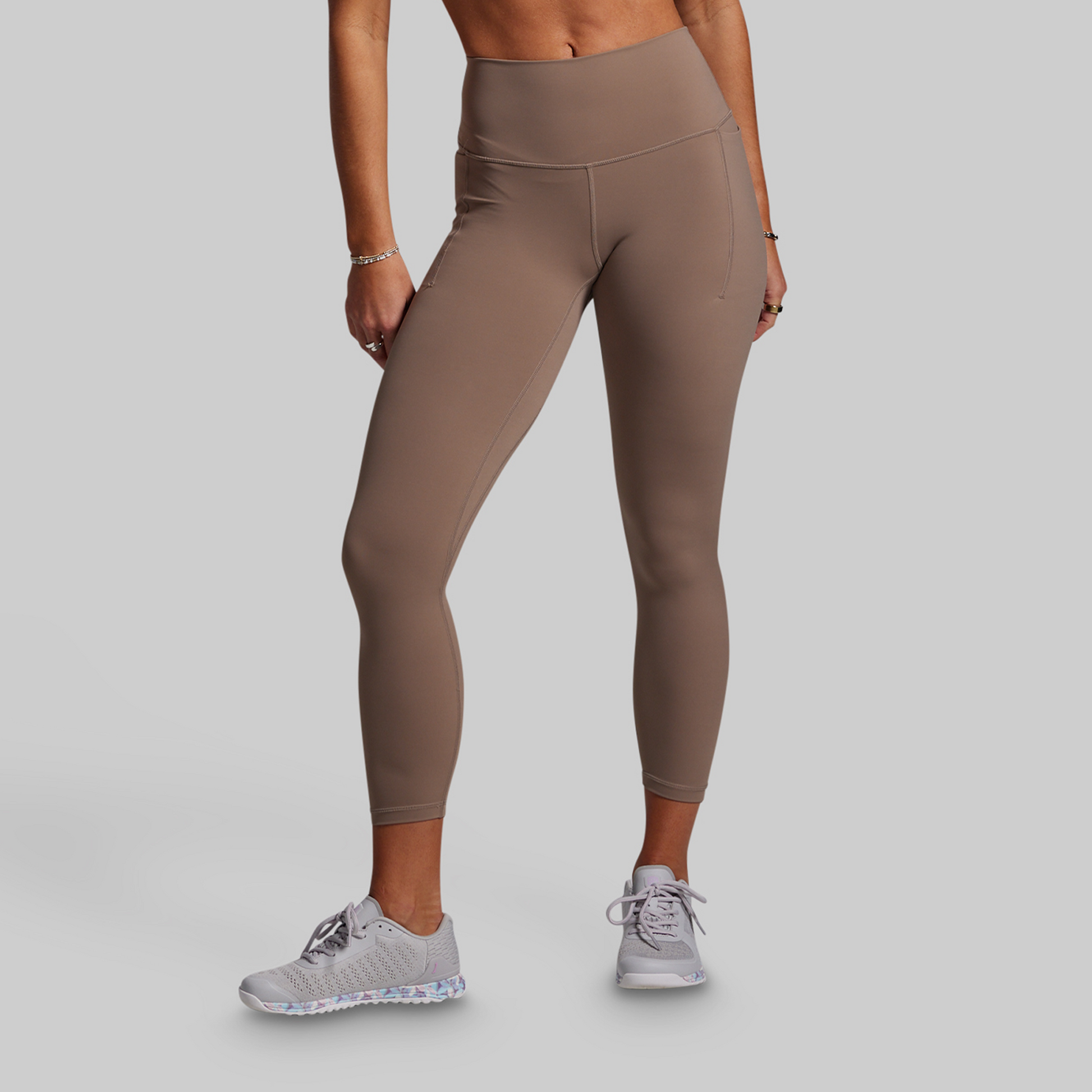 Person wearing beige leggings and white sneakers on a gray background