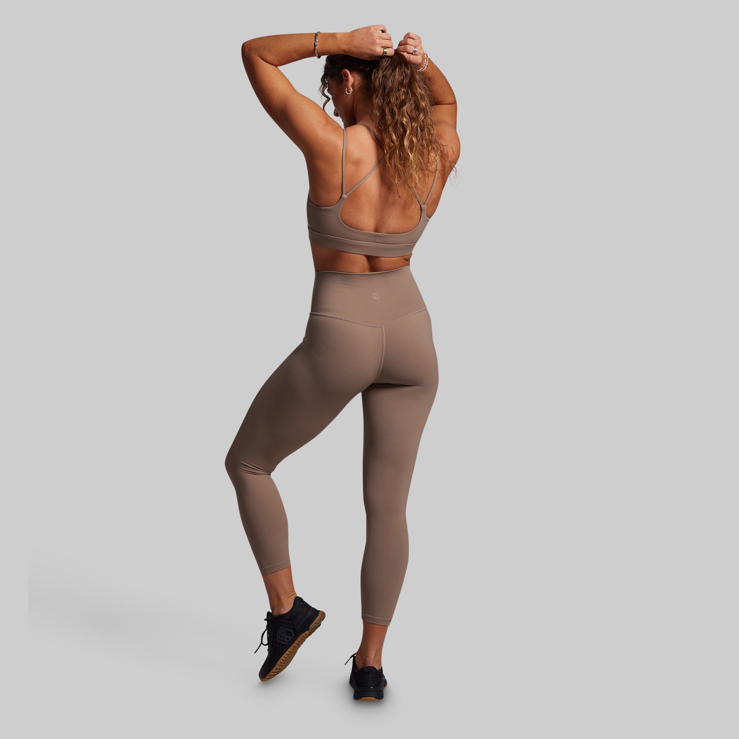 Woman wearing a brown sports bra and leggings on a gray background