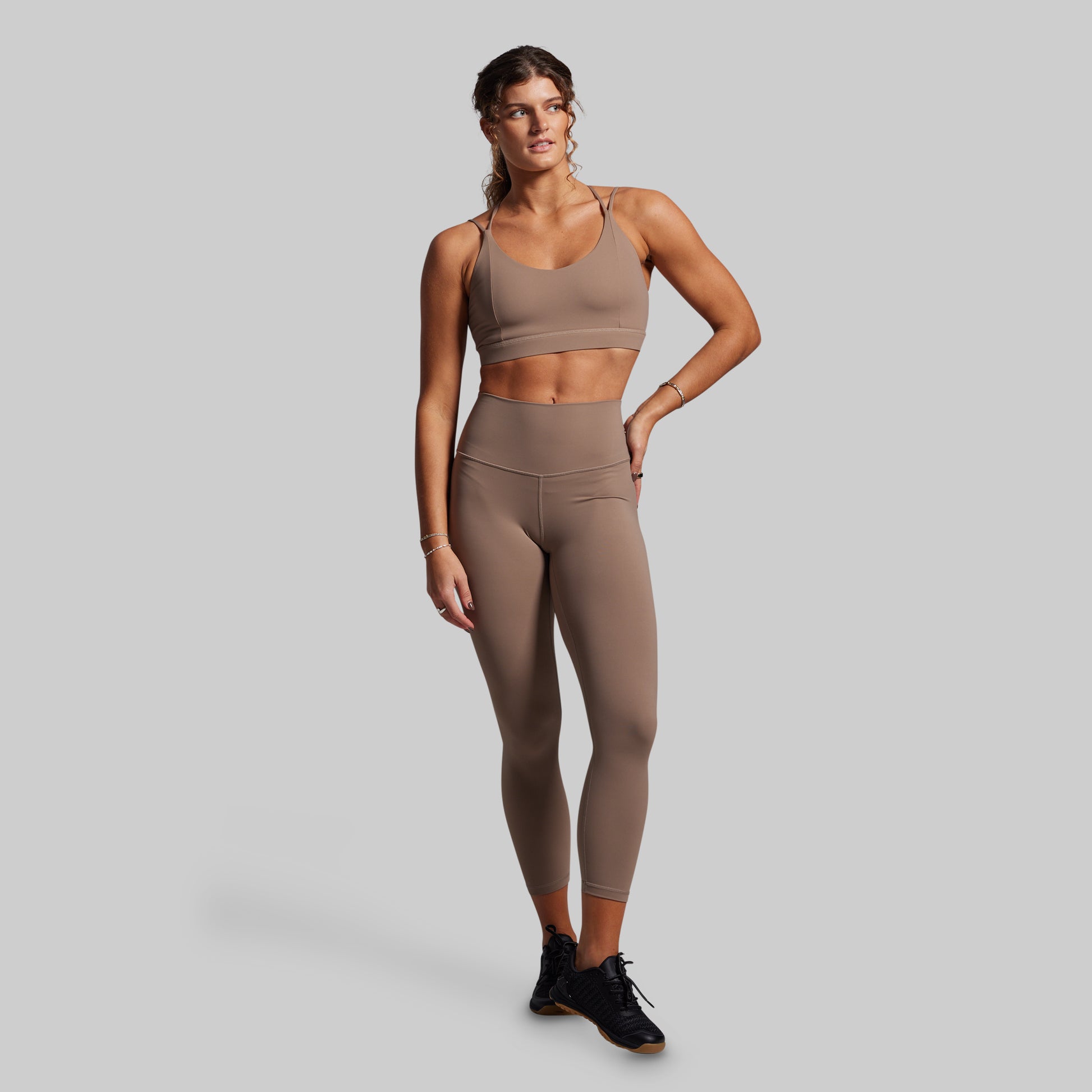 Woman wearing a brown sports bra and leggings set on a gray background