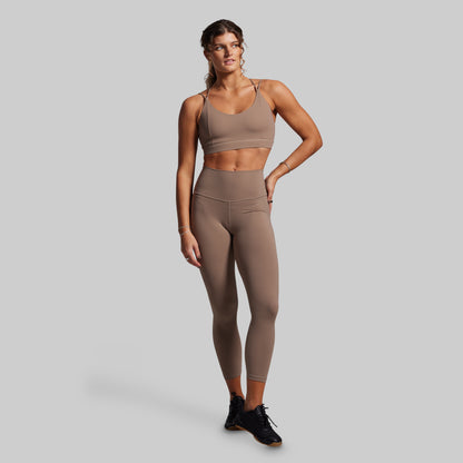 Woman wearing a brown sports bra and leggings set on a gray background