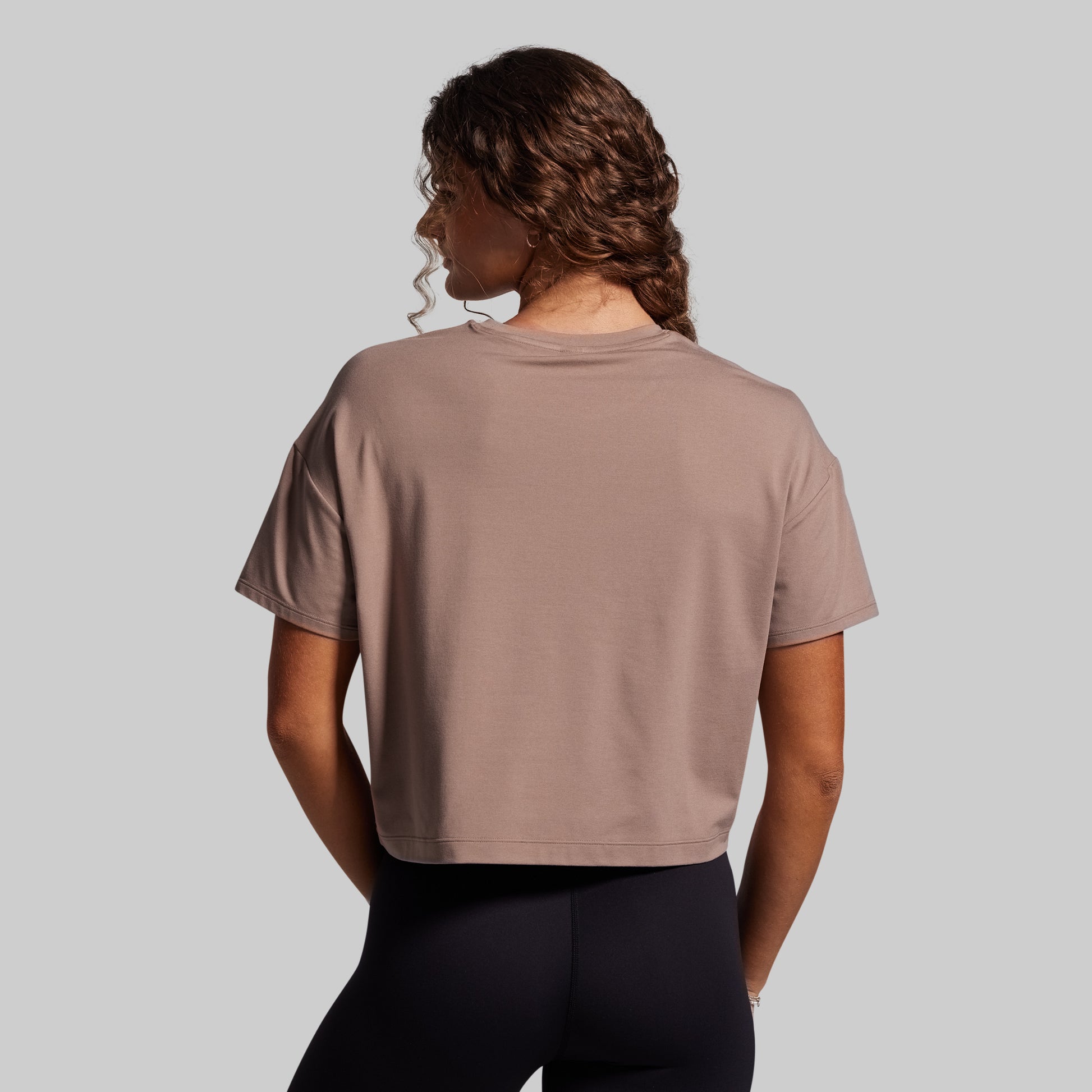 Person wearing a beige t-shirt and black leggings on a gray background