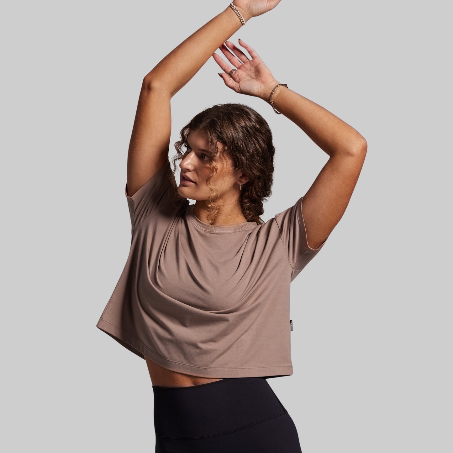 Woman wearing a brown t-shirt and black leggings against a gray background