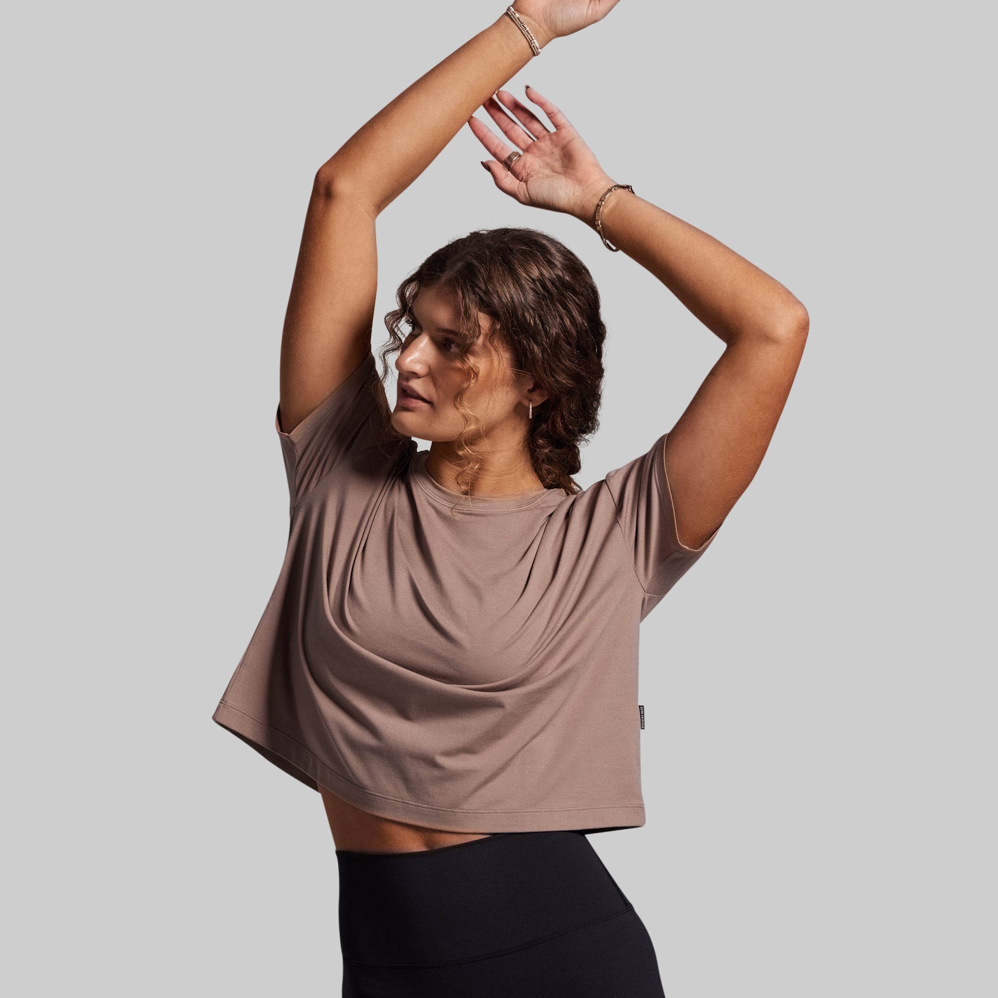 Woman wearing a brown t-shirt and black leggings against a gray background