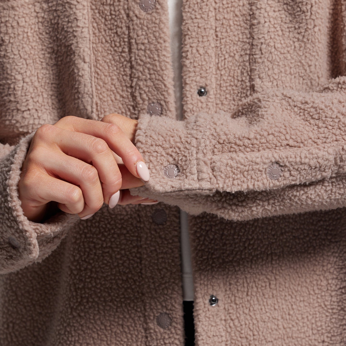 Close-up of a person wearing a brown sherpa jacket with a blurred background