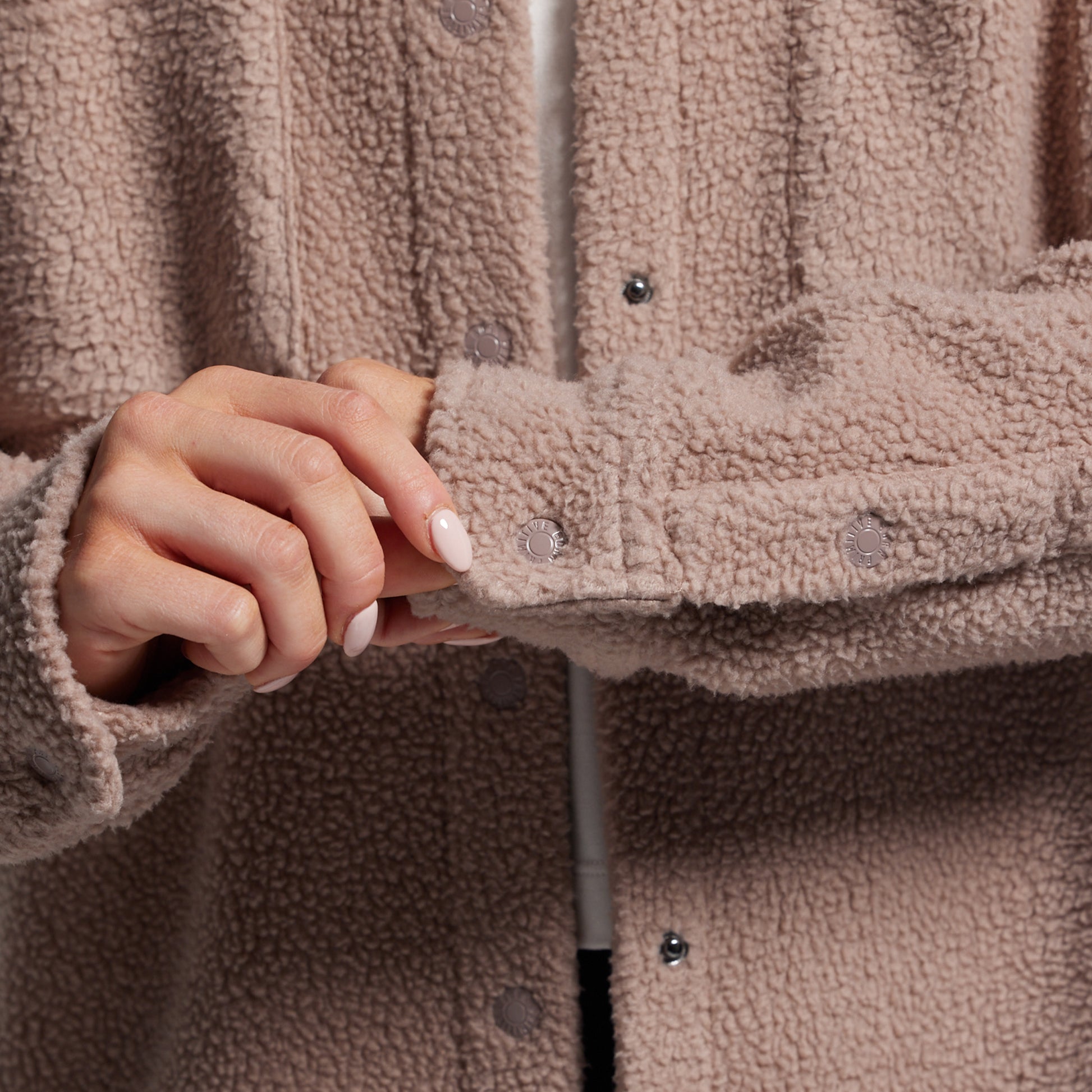 Close-up of a person wearing a brown sherpa jacket with a blurred background