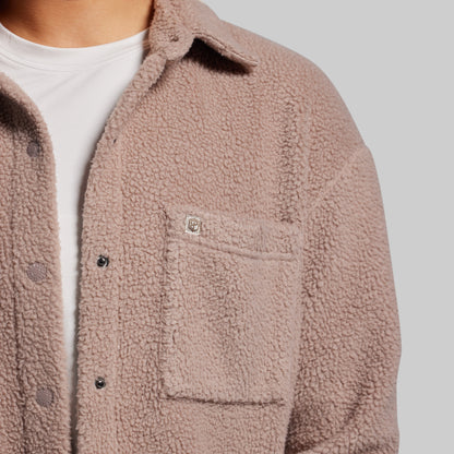 Close-up of a person wearing a brown sherpa jacket on a gray background