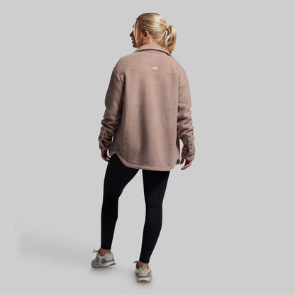 Person wearing a brown jacket and black leggings on a gray background