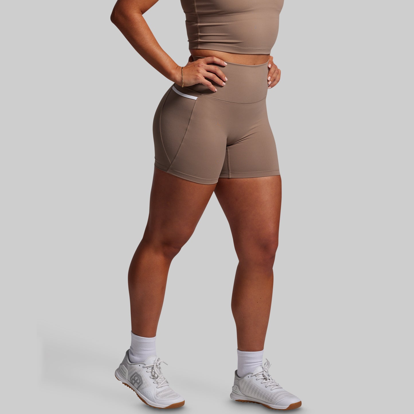 Person wearing brown athletic shorts and a matching sports bra on a gray background