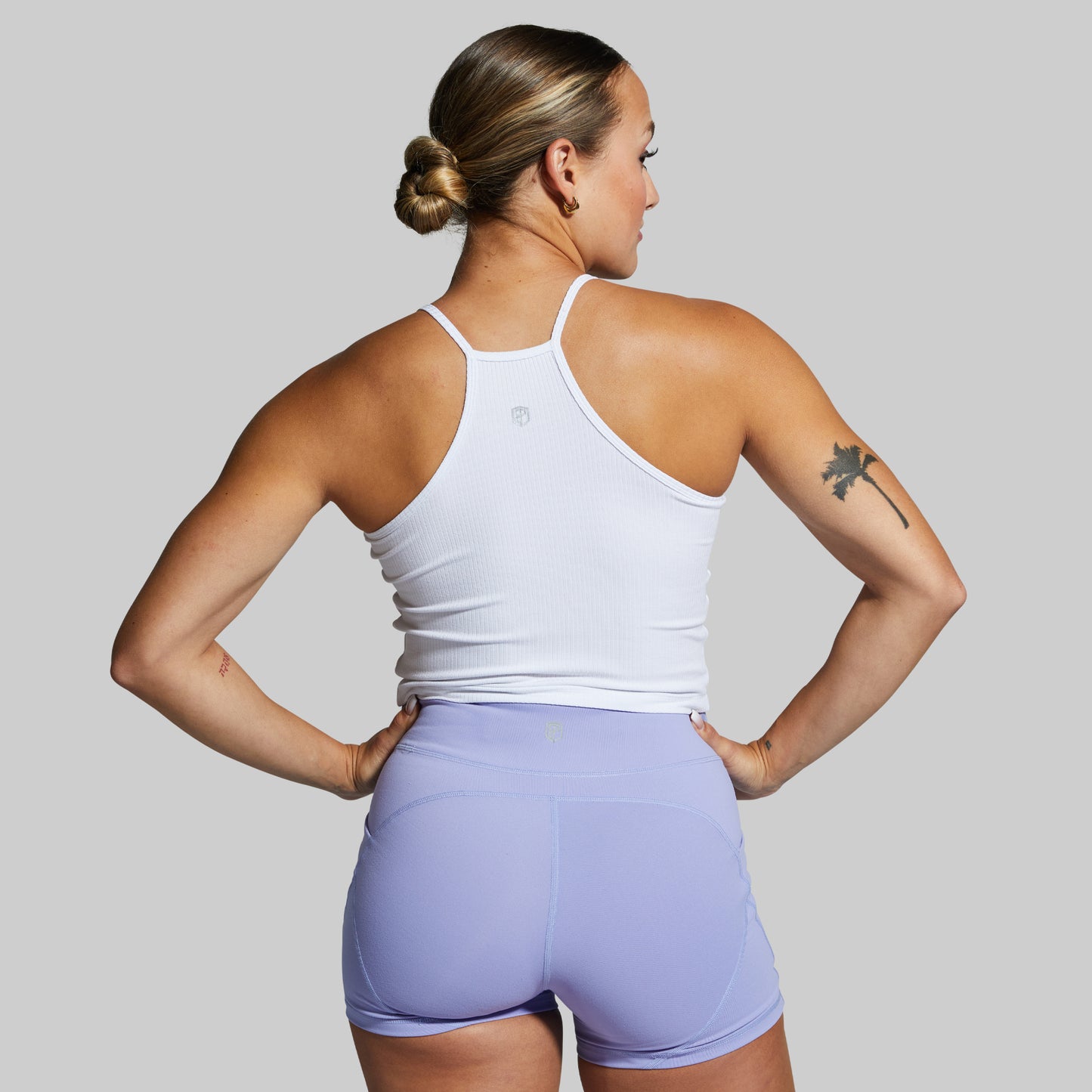 Woman wearing a white tank top and light purple shorts on a gray background