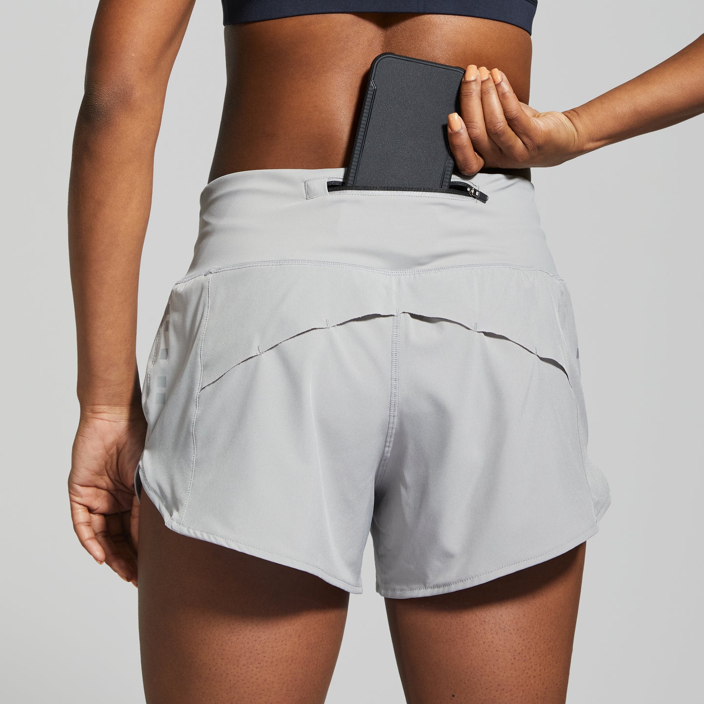 Person wearing light gray athletic shorts with a phone case in a pocket on a plain background