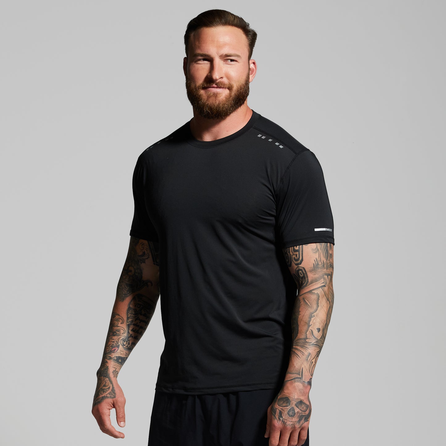 Man wearing a black athletic shirt with visible tattoos on arms against a gray background